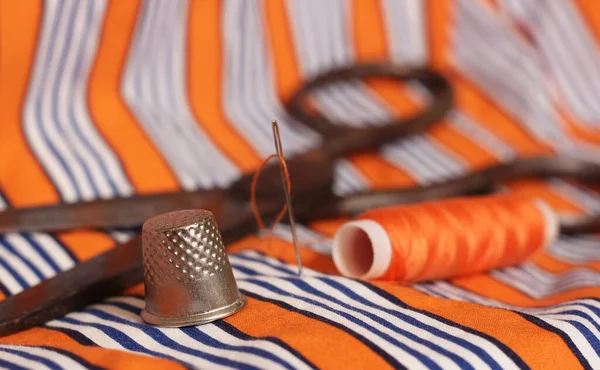 Linha laranja e dedal em tecido listrado laranja e branco — Fotografia de Stock