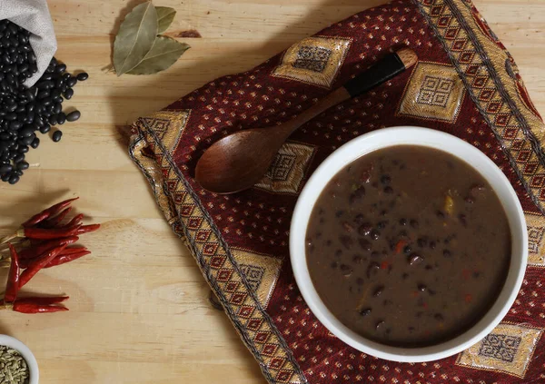 Baharatlı ve kuru fasulyeli, ahşap masadaki siyah fasulye. Kasenin altında eski kumaş