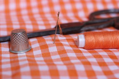 Portakal rengi ve beyaz kareli kumaş. Yüksük ve turuncu iplikli. Arkaplanda Klasik Makas