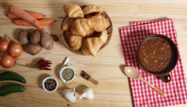 Ahşap masa üzerinde kırmızı ve beyaz kareli kumaşlı sığır güveci ve taze ekmek.