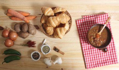 Ahşap masa üzerinde kırmızı ve beyaz kareli kumaşlı sığır güveci ve taze ekmek.