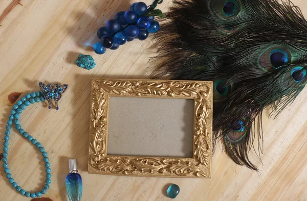 Blue Jewelry and Peacock Feathers With Gold Picture Frame on Wood Background
