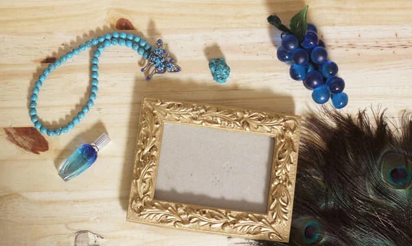 Blue Jewelry and Peacock Feathers With Gold Picture Frame on Wood Background