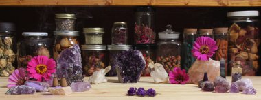 Amethyst Crystals and Flowers On Meditation Table With Jars of Dried Herbs in Background