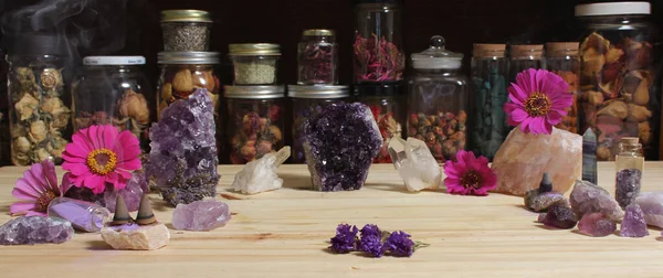 Amethyst Crystals and Flowers On Meditation Table With Jars of Dried Herbs in Background