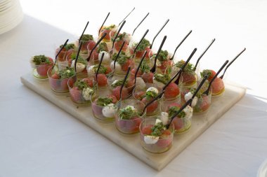 Küçük nefis İtalyan vejetaryen ısırığı, soyulmuş domates, mozzarella peyniri ve fesleğen pesto aperatiflerini şeffaf plastik bardaklarda tepside kapatıyoruz.