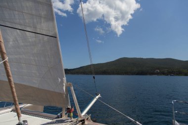Deniz, adalar, pelerinler, beyaz bulutlar ve mavi gökyüzü olan bir katamaran yat teknesinin gündüz görüşü. Rusya 'nın Vladivostok kentindeki Russky adasındaki Novik limanı