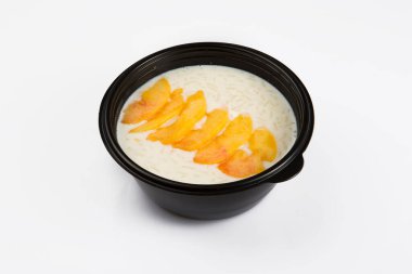 Üst köşeden izole edilmiş beyaz pirinç sütlü lapanın beyaz arka planda siyah plastik bir kasede şeftali dilimleri ile çekilmiş görüntüsü.