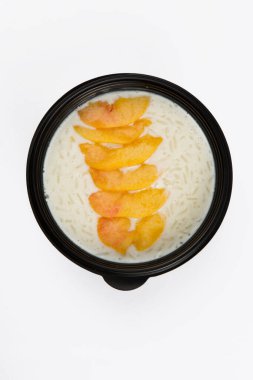 Beyaz arka planda siyah plastik bir kasede şeftali dilimleri ile lezzetli beyaz pirinç sütlü lapanın yakın çekim görüntüsünü izole ettim.