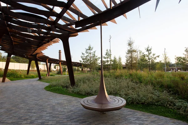 dönen ahşap bank ve metal pergola. Çimenli yol, çalılar, bitkiler, arka planda ağaçlar. Tyufeleva Roshcha şehir parkı, Zilart, Moskova, Rusya. ! melk peyzaj mimarisi şehir tasarımı