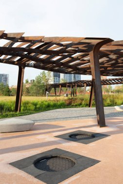 Arkasında metal pergola olan çocukların oyun parkındaki trambolinler ve üçgen banklar. Tyufeleva Roshcha şehir parkı, Zilart! Melk peyzaj mimarisi şehir tasarımı