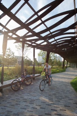 Moskova, Rusya - 08.08.2021 sıralı bir adam, baba, bisikletli bir çocuk korse çelik pergola, çimen, ağaçların altında. Tyufeleva Roshcha Parkı, Zilart. ! melk peyzaj mimarisi şehir tasarımı
