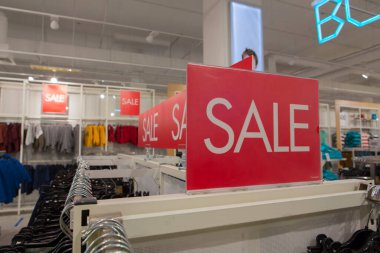 Bir giyim mağazasında beyaz harflerle yazılmış kırmızı dikdörtgen panolarda indirimli satış tabelaları