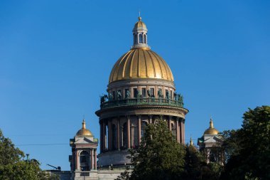 SAINT PETERSBURG, RUSSIA 13.08.2021 Saint Isaac's Cathedral golden cupola dome, granite columns, statues behind green trees foliage close up shot on blue sky background