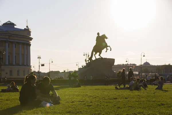 SAINT PETERSBURG, RUSSIA 13.08.2021 contrast shot of people sitting on grass in Alexander Garden park with silhouette of Bronze Horseman sculpture of Peter the Great on blue sky and sun background