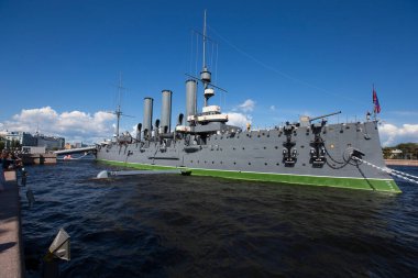 SAINT PETERSBURG, RUSSIA 13.08.2021 side view of Cruiser Aurora with naval jack flag and forecastle gun on a summer day blue sky background. Vessel moored and anchored at Neva river embankment