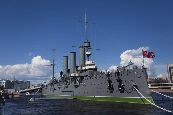 SAINT PETERSBURG, RUSSIA 13.08.2021 side view of Cruiser Aurora with naval jack flag and forecastle gun on a summer day blue sky background. Vessel moored and anchored at Neva river embankment