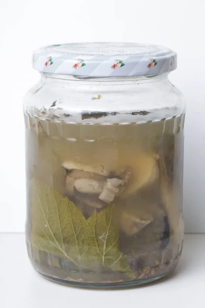 酢漬けのポルチーニキノコとグラスマソン瓶のブドウの葉は蓋で閉じることができます 白い背景の上に垂直に隔離された — ストック写真