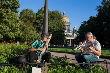 SAINT PETERSBURG, RUSSIA 13.08.2021 Sokak müzisyenleri Chapman Stick müzik enstrümanı, trompet ve hava tüpü melodileri çalıyor Alexander Garden 'da, St. Isaac Katedrali arkada..