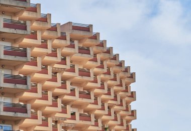 Merdivenler, balkonlu ve mavi gökyüzü ve bulutlu pencereli bir tatil binası.