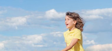 Genç yakışıklı çocuk gülerken yukarı bakıyor ve zıplıyor ve oynuyor. Mavi gökyüzü arka planı. Boşluğu kopyala