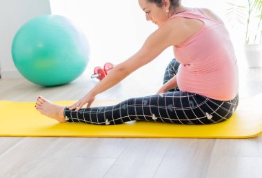 Genç hamile kadın spor paspası üzerinde egzersiz yapıyor. Arka planda spor topu ve halterler var. hamilelik sağlığı konsepti