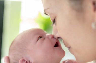 Annesi burnunu onunkine yaklaştırdığında gülen ve ağzını açan yeni doğmuş bir bebek. konsept bakım, şefkat ve yeni doğan bebeğin korunması