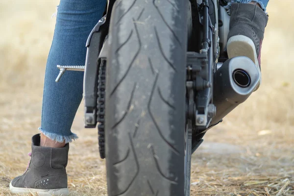 道路のバイクの車輪の後部ビュー バイクに乗るための安全ブーツを身に着けているバイカーの女性の足と保護とジーンズ — ストック写真