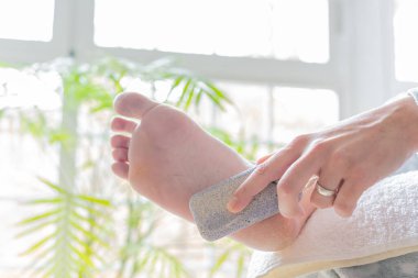 Ayaklarındaki nasırları yumuşatmak için sünger taşı kullanan genç bir kadının elleri. konsept vücut bakımı, pedikür ve ayak refleksolojisi