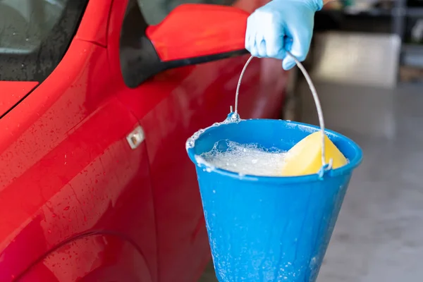 man\'s hand holding a bucket with soap to wash his car