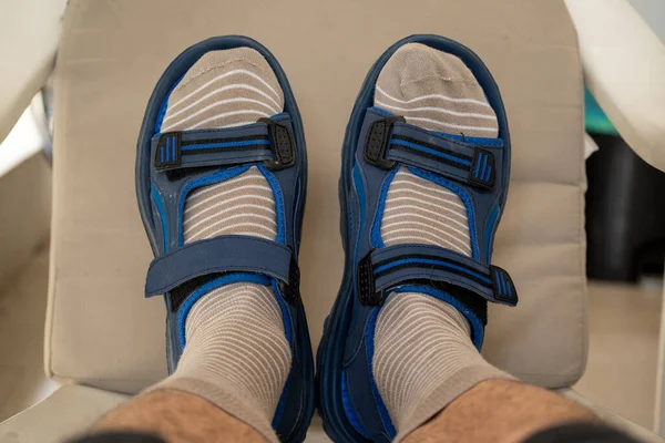 Close up of a man\'s feet on a plastic chair wearing beige socks with white stripes and sandals.