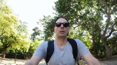A man with sunglasses rides a bike at the park .Low angle footage with sky and trees at the background.