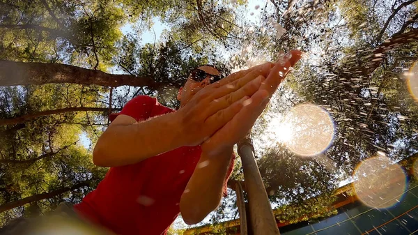Low angle footage shows a man washes his hands under an open faucet outdoors. Trees and sky at the background.