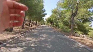 Footage shows a man running on an uphill road in a park. Pov video.