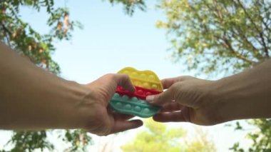 Pov footage from low angle view show the hands of a person playing with an  anti stress fidget bubble pop toy outdoors. Sky and trees at the background.