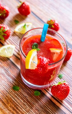 Tahta arka planda limonlu, naneli ve mavi pipetli taze çilekli smoothie. Sağlıklı yaşam tarzı kavramı.