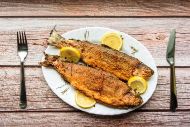 Lezzetli kızarmış balık, limon ve baharatlı beyaz tabak. Ahşap arka plan. Üst görünüm.