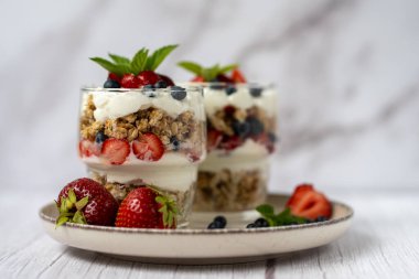 Bir bardak granola, yoğurt ve beyaz masada taze çilek. Sağlıklı kahvaltı kasesi konsepti. Yüksek kalite fotoğraf