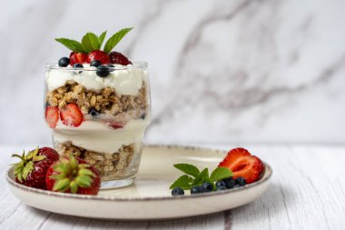 Bir bardak granola, yoğurt ve beyaz masada taze çilek. Sağlıklı kahvaltı kasesi konsepti. Yüksek kalite fotoğraf