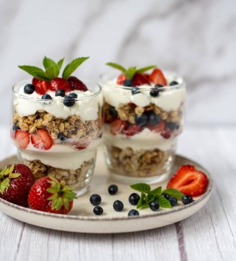 Bir bardak granola, yoğurt ve beyaz masada taze çilek. Sağlıklı kahvaltı kasesi konsepti. Yüksek kalite fotoğraf