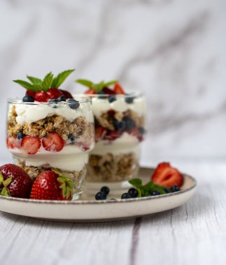 Bir bardak granola, yoğurt ve beyaz masada taze çilek. Sağlıklı kahvaltı kasesi konsepti. Yüksek kalite fotoğraf