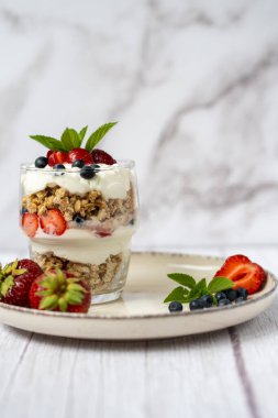 Bir bardak granola, yoğurt ve beyaz masada taze çilek. Sağlıklı kahvaltı kasesi konsepti. Yüksek kalite fotoğraf