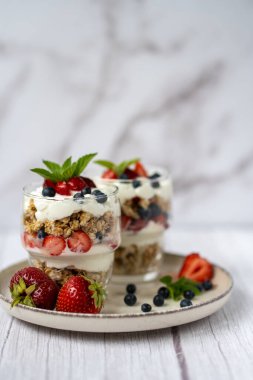 Bir bardak granola, yoğurt ve beyaz masada taze çilek. Sağlıklı kahvaltı kasesi konsepti. Yüksek kalite fotoğraf