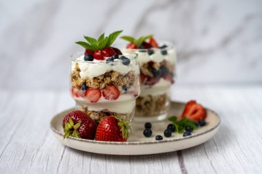 Bir bardak granola, yoğurt ve beyaz masada taze çilek. Sağlıklı kahvaltı kasesi konsepti. Yüksek kalite fotoğraf