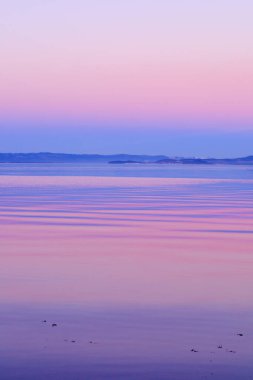 Mavi deniz ya da fiyort okyanusunun üzerinde parlayan pembe bulutlarla birlikte renkli günbatımı gökyüzü. Sudaki yansımalar. Nefes kesici bir manzara. Romantik manzara. Doğada güzellik