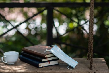 Coronavirus salgını sırasında ders almak ve anlamak için üç kitap, bir maske ve bir içecek ahşap bir masaya yerleştirilir. Salgın sırasında evden öğreniyorum.