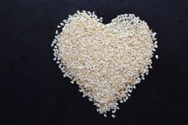 Beyaz bir masaya yığılmış susam tohumları sağlık ve sağlık kavramı olarak kalp şeklinde yapılır. Kalp şeklinde sıralanmış organik susam tohumu, sağlık hizmetlerini temsil eder..