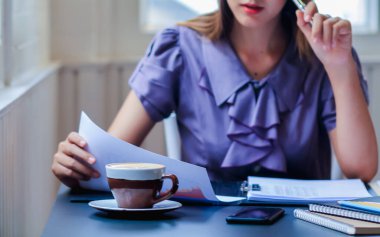 Bir muhasebeci, yıllık sonuçlarını özetlemek için masalarının üzerinde duran büyük miktarda gelir ve gider belgelerini inceliyor. Kazancı özetlemek için muhasebe kavramları