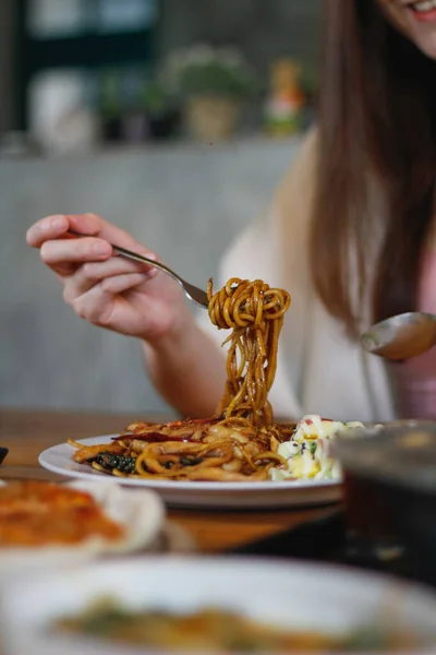 Asian woman eating spaghetti with spicy seafood sauce in a restaurant. The spicy seafood spaghetti was served in a plate and placed on the dining table as the woman ordered.