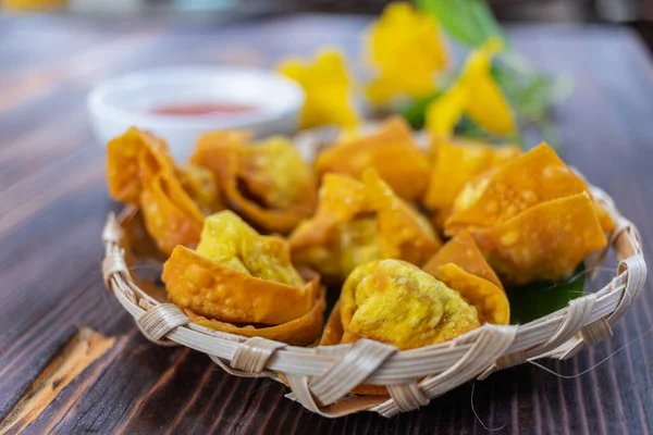 Crispy dumplings wrapped in chicken, vegetables and spices are served in a white plate placed on a wooden table inside the restaurant. Fried dumplings are popular for their delicious taste.